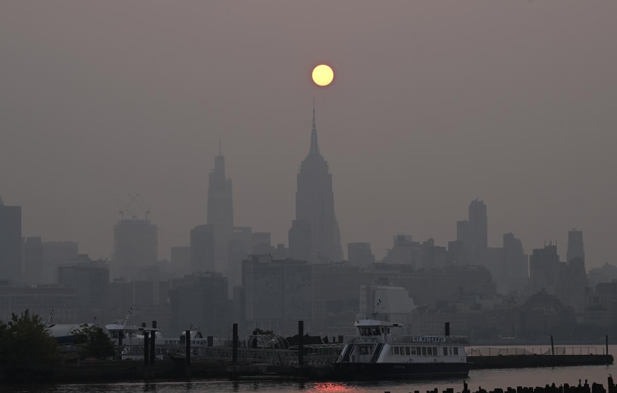 an orange sun hangs above skyscrapers on a very smoky day