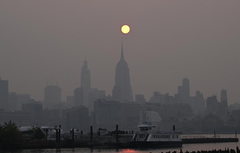 an orange sun hangs above skyscrapers on a very smoky day