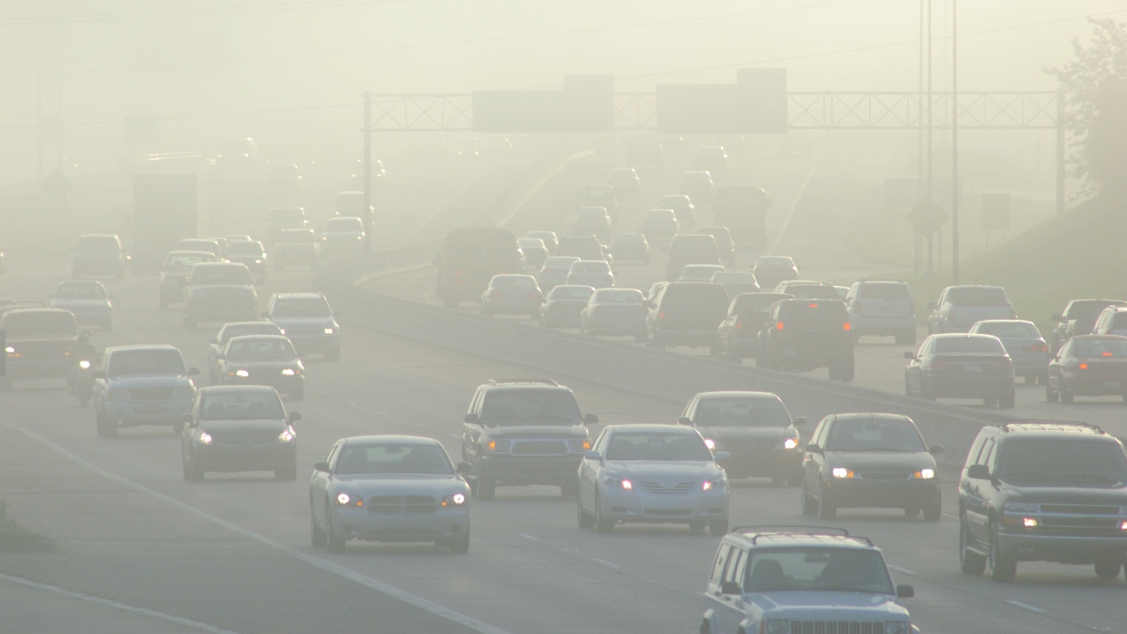 Cars drive navigate traffic and smog on a large highway during rush hour.