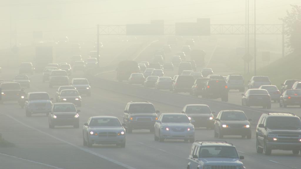 Cars drive navigate traffic and smog on a large highway during rush hour.