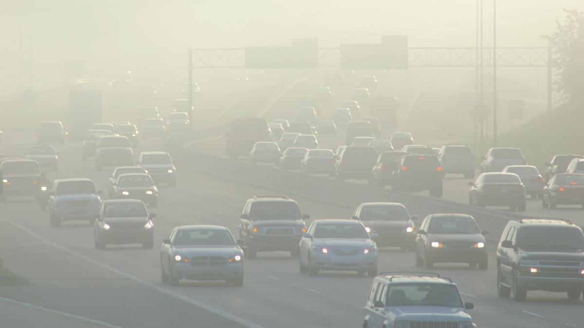 Cars drive navigate traffic and smog on a large highway during rush hour.