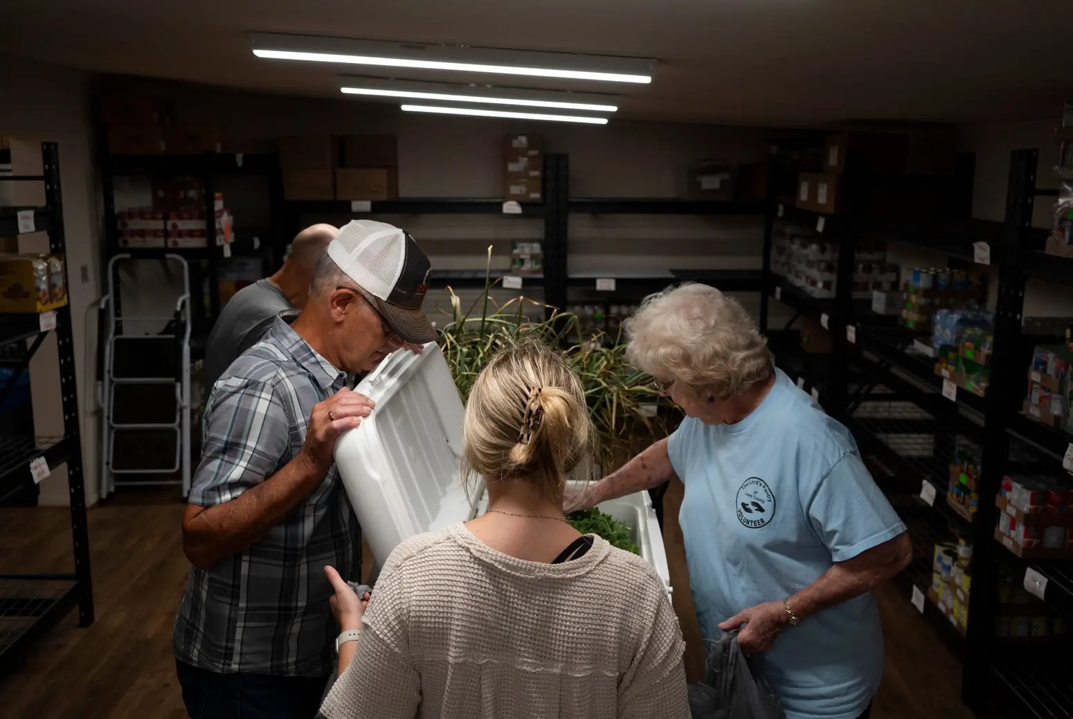 A group of people gather around an open box in a storage room.