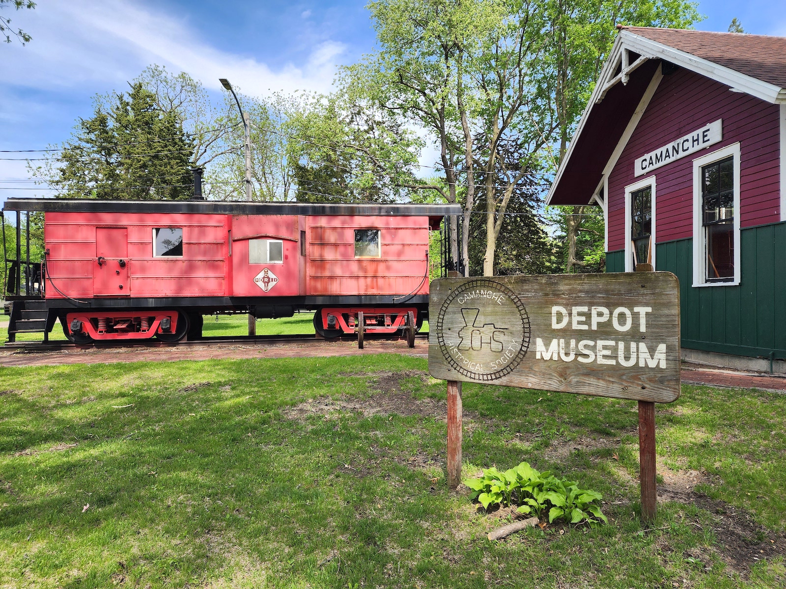 A red train car sits outside of the Camanche Historical Society Depot Museum.