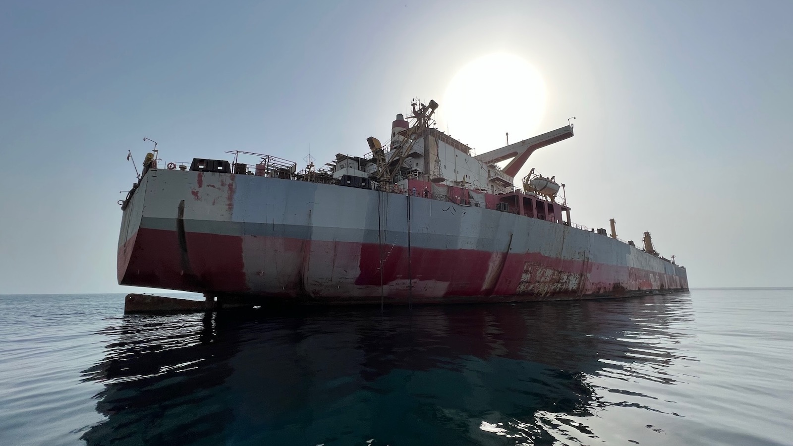 A rusting and decaying oil tanker called the FSO Safer is seen in the Red Sea with the sun shining brightly directly above it.
