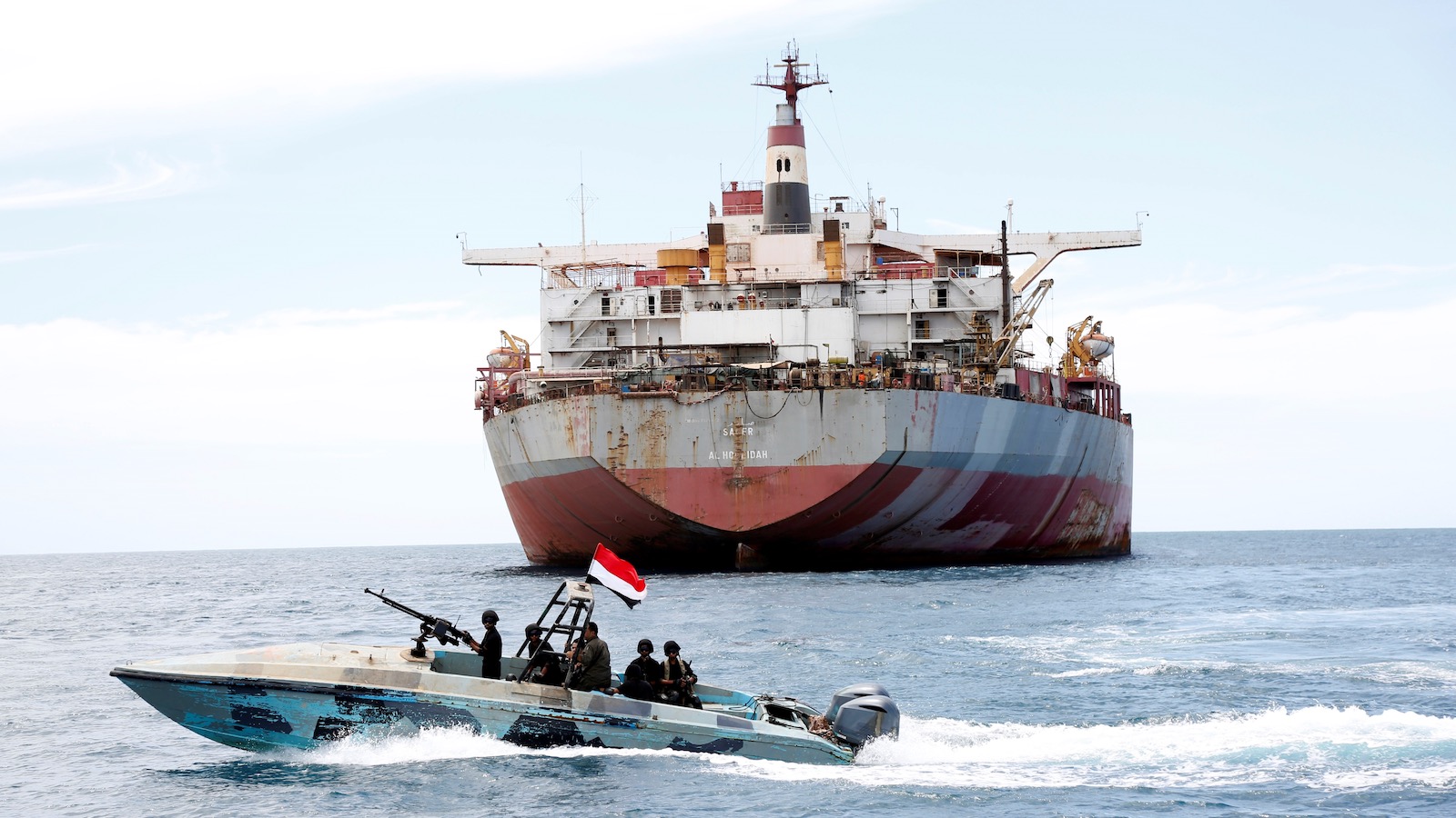 A black and blue speedboat with a machine gun on its deck patrols the area around the rusty and decaying oil tanker FSO Safer on the Red Sea.