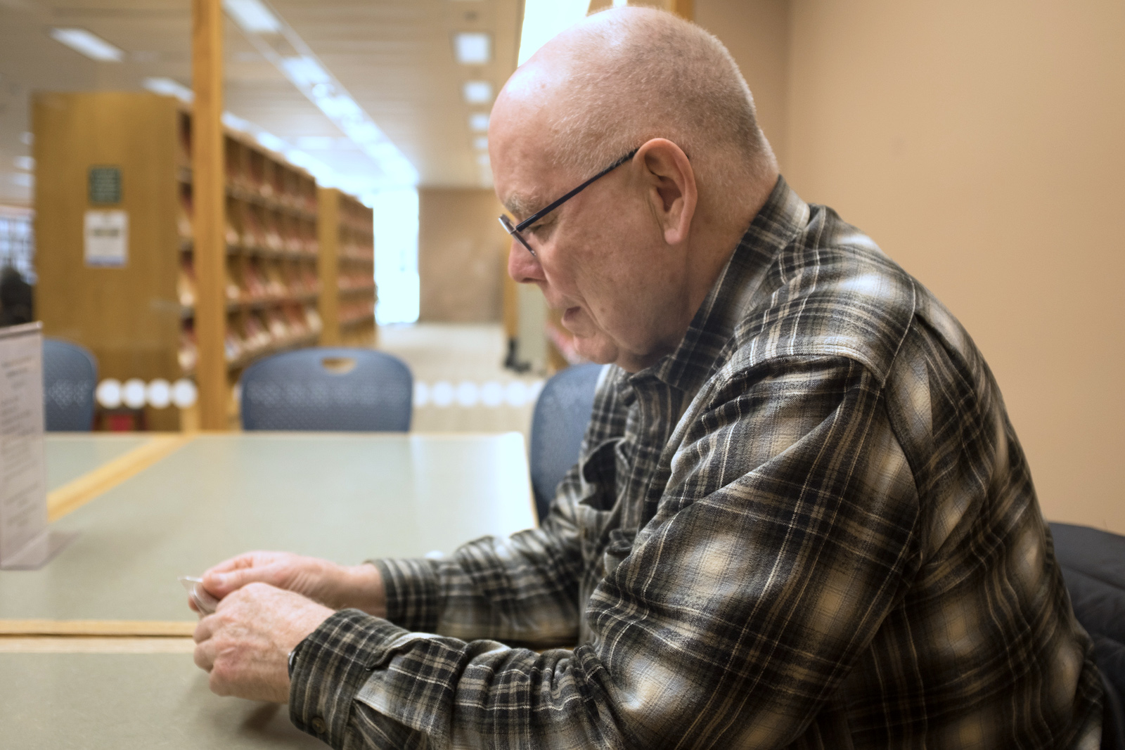 a man in a flannel shirt sits in a library looking at his hands