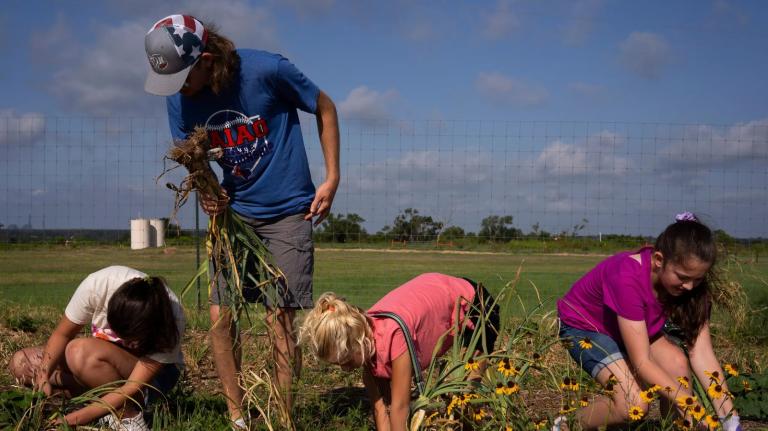 A man and three children stand in a garden in front of green fields.