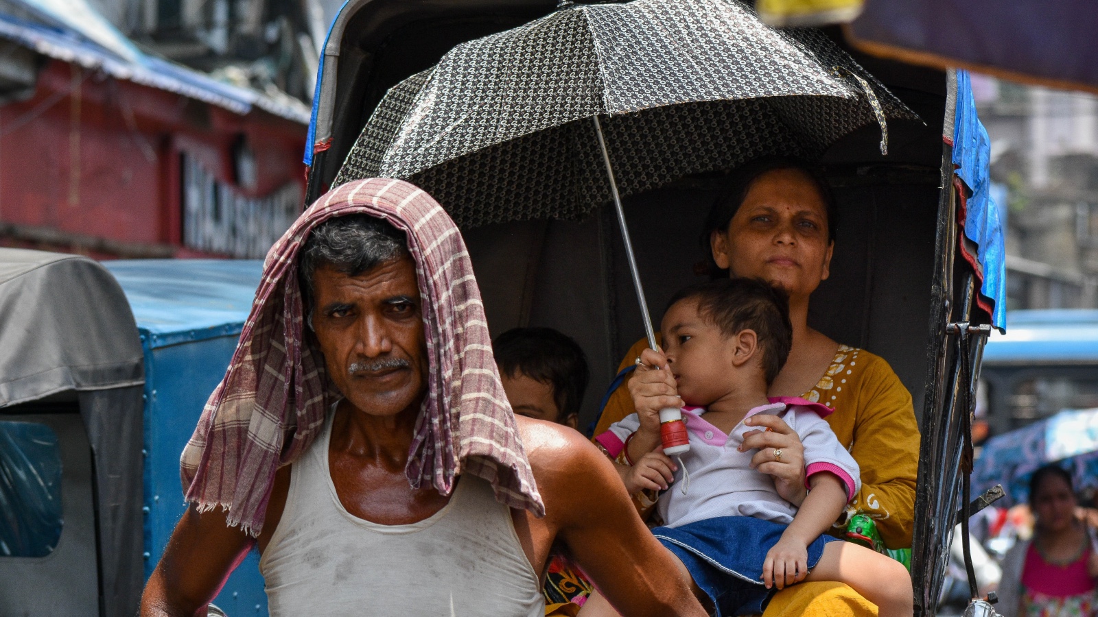 A man drapes a cloth over his head and a mother holds an umbrella over her child inside a hand pulled rickshaw to escape from extreme heat in India
