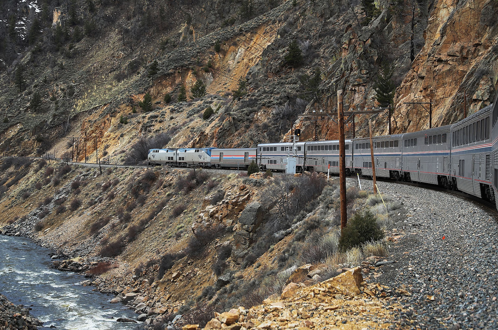 a passenger train runs alongside a rocky cliff face