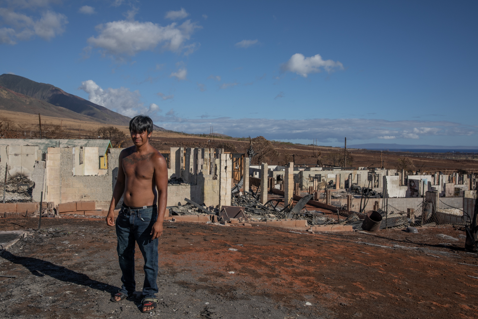 a shirtless man stands in a burned neighborhood
