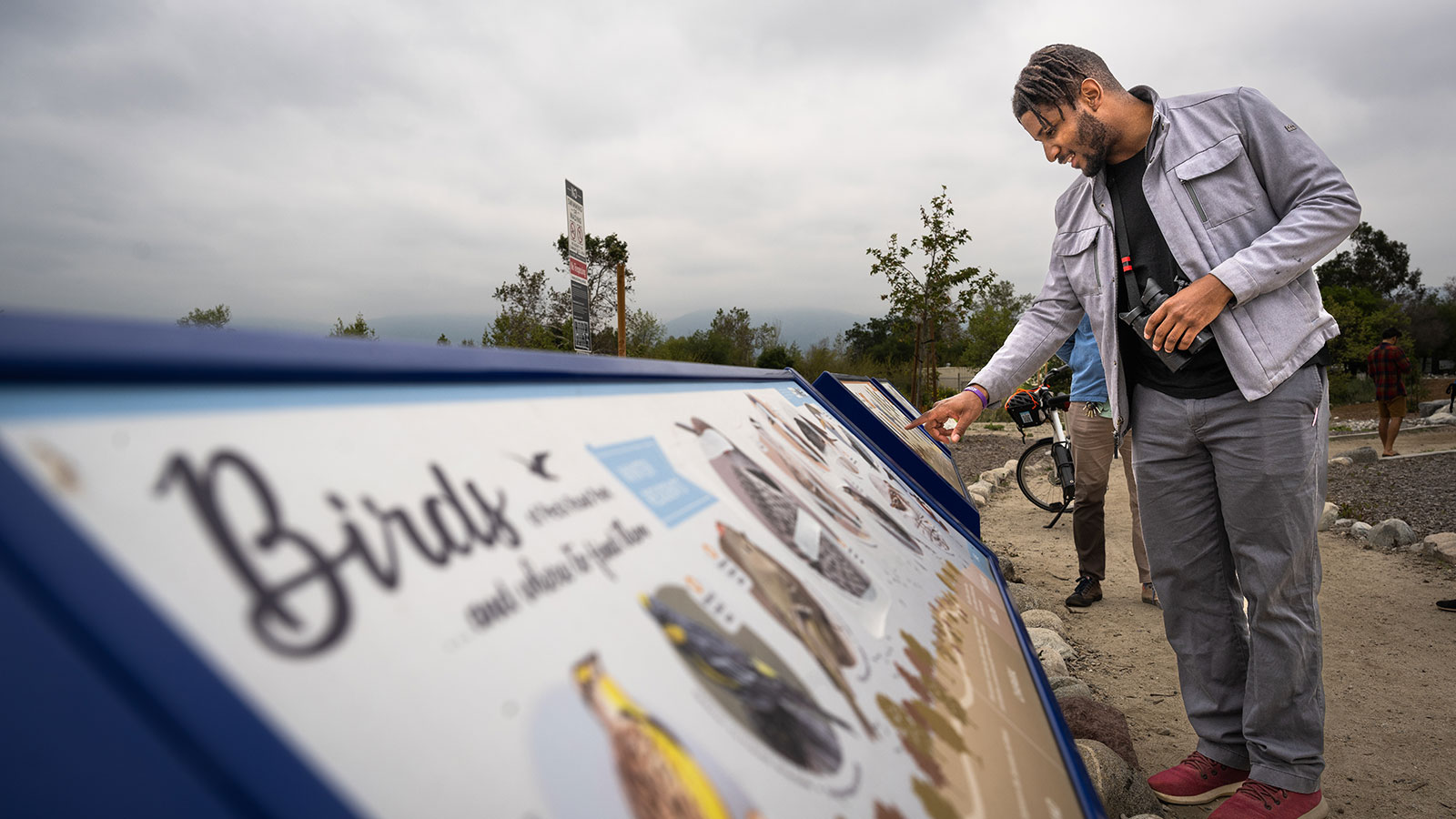 A man with binoculars studies a sign with information about local birds