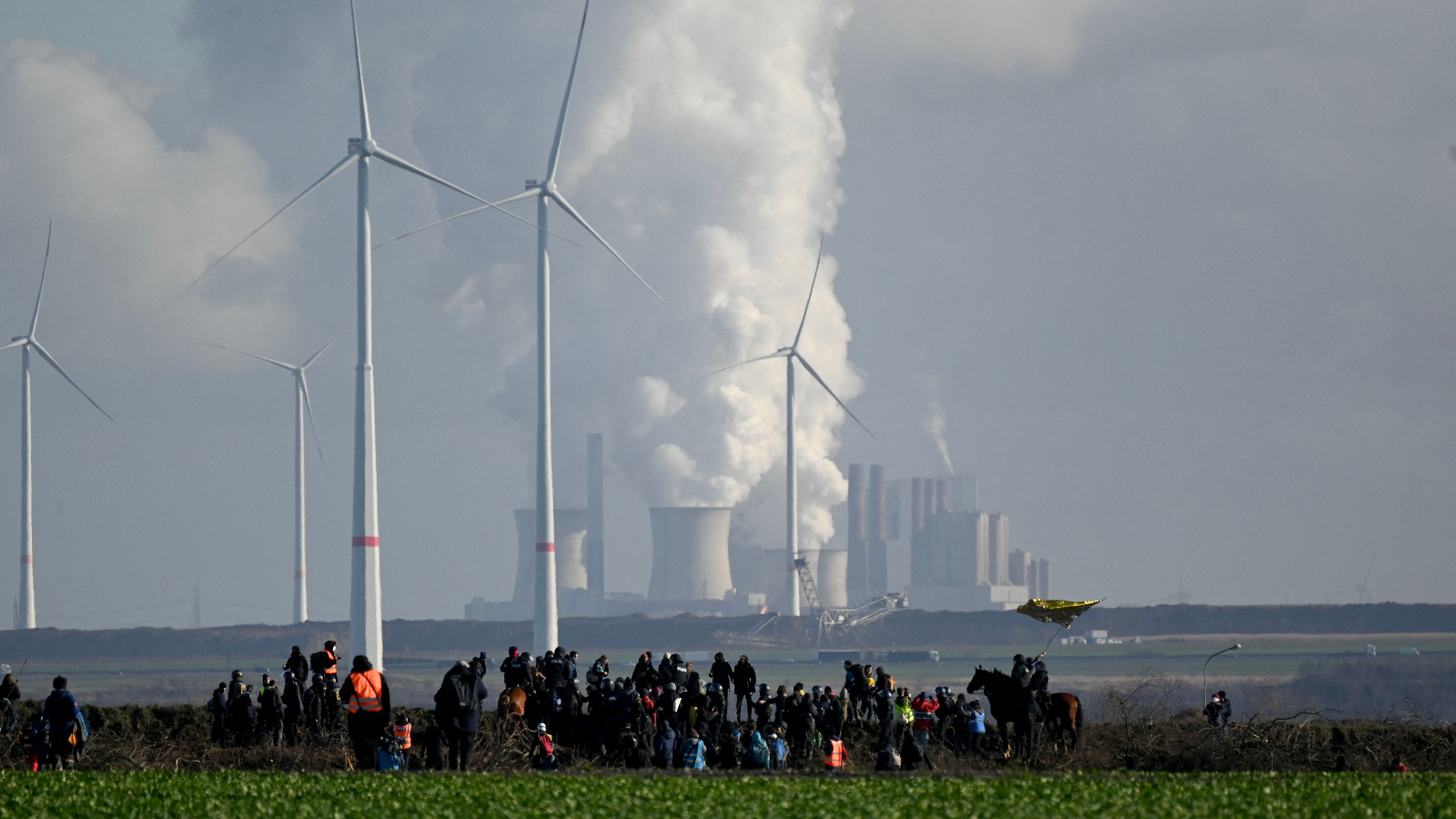 Photo of a group gathering in front of a backdrop of industrial smokestacks and wind turbines