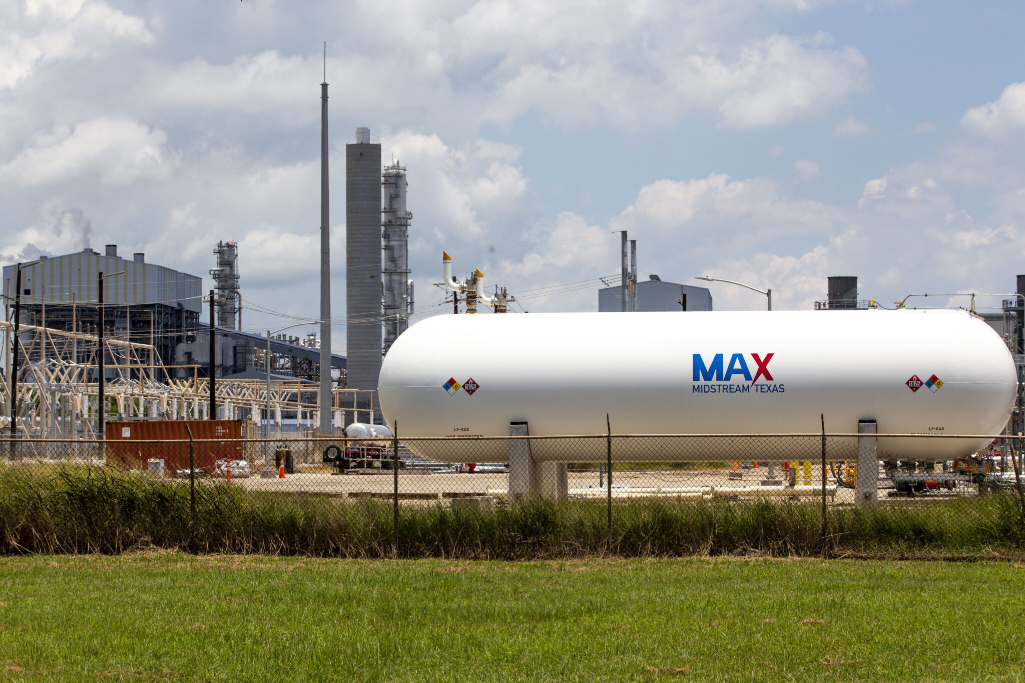 A white tank that says Max sits in front of a refinery.
