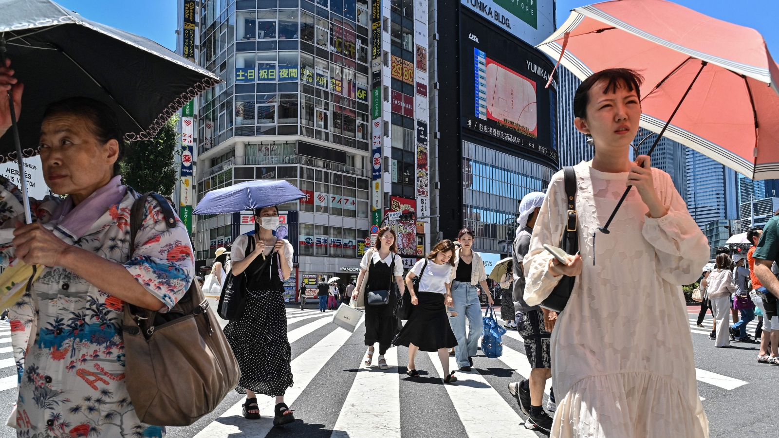 People using umbrellas and parasols to seek relief from the heat while crossing a street in Tokyo.