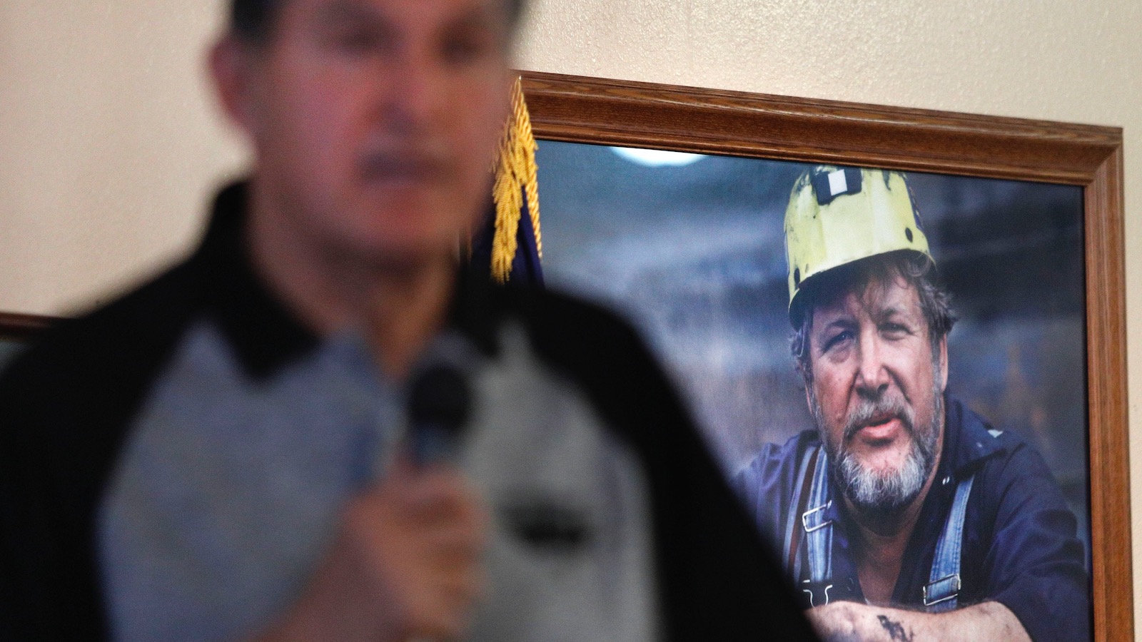 Senator Joe Manchin of West Virginia addresses a crowd while standing in front of a portrait of a coal miner.