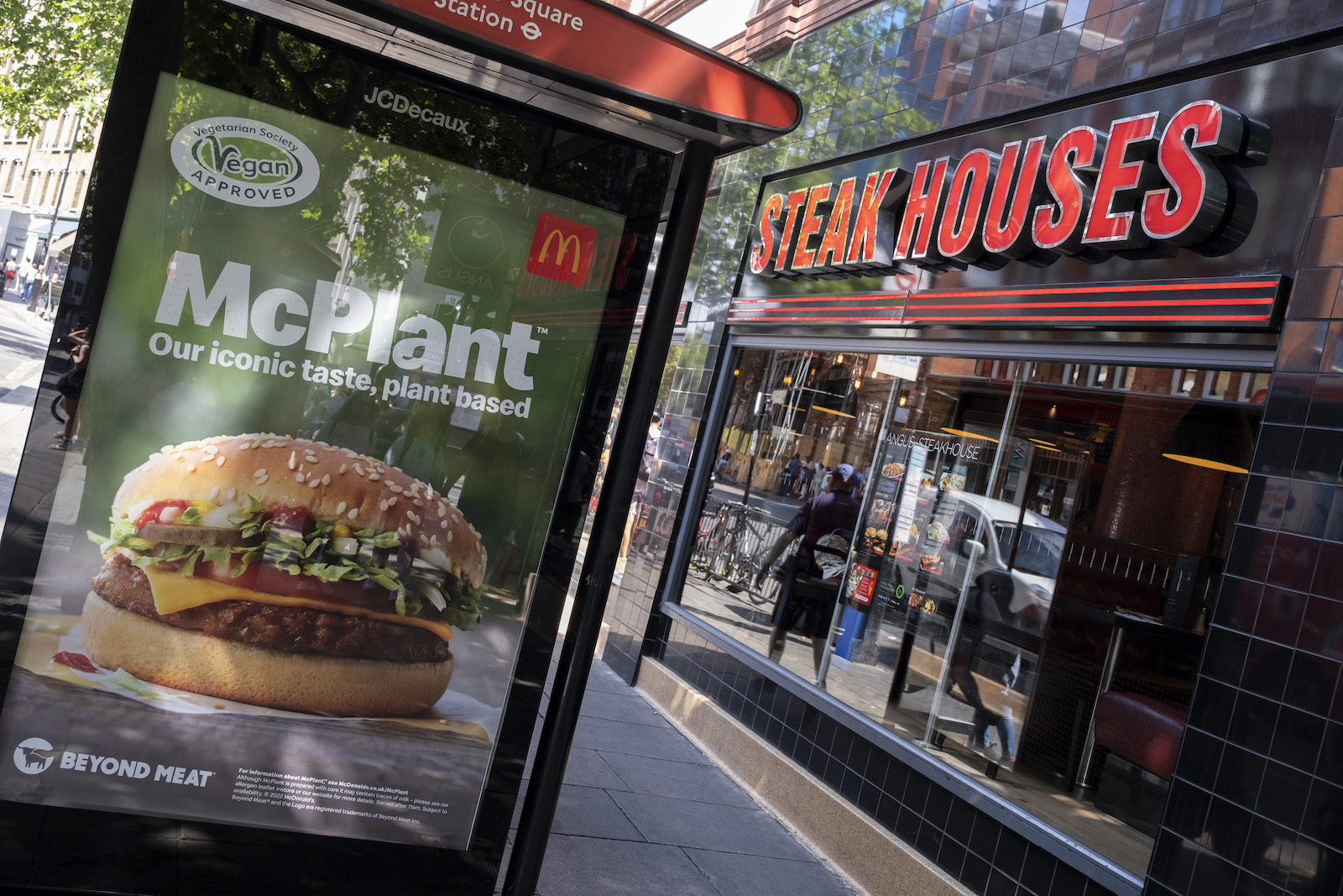 a bus station ad for a plant-based meat burger from McDonalds outside of a steak restaurant
