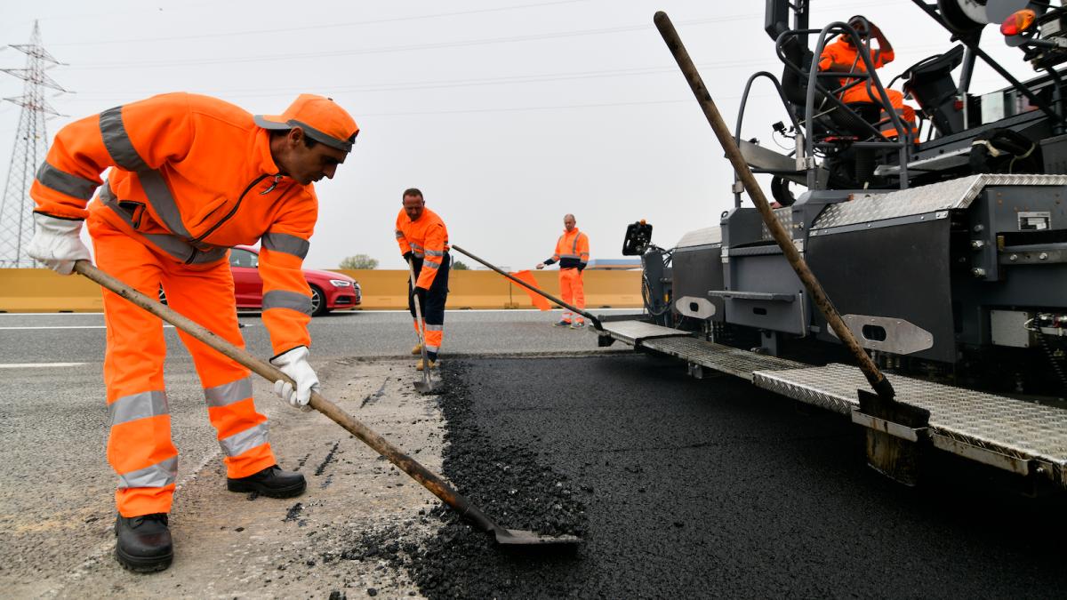 Workers lay down plastic-infused asphalt