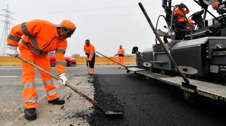 Workers lay down plastic-infused asphalt