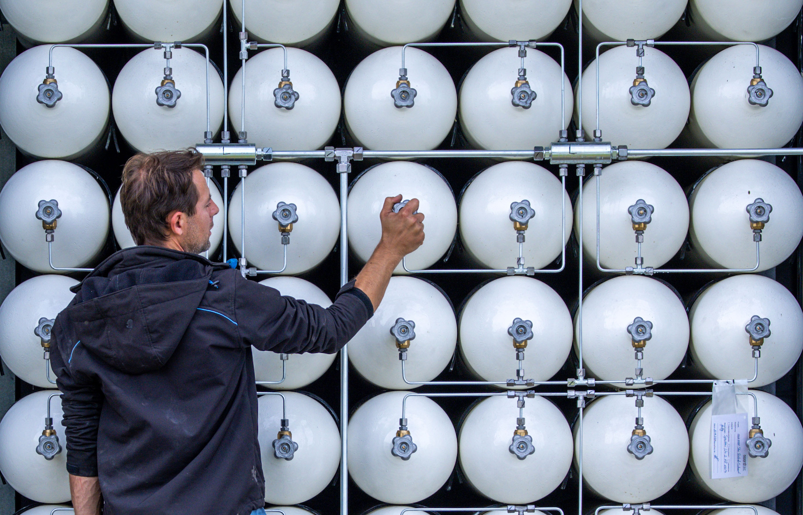 a man checks a stacked gas canister on a wall full of canisters
