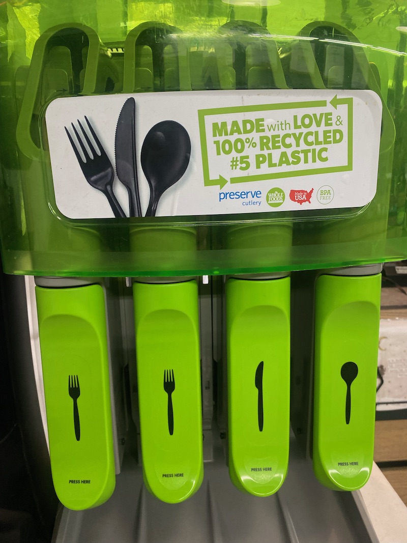 a bright green dispenser for plastic forks knives and spoons that says the utensils are made from 100% recycled plastic