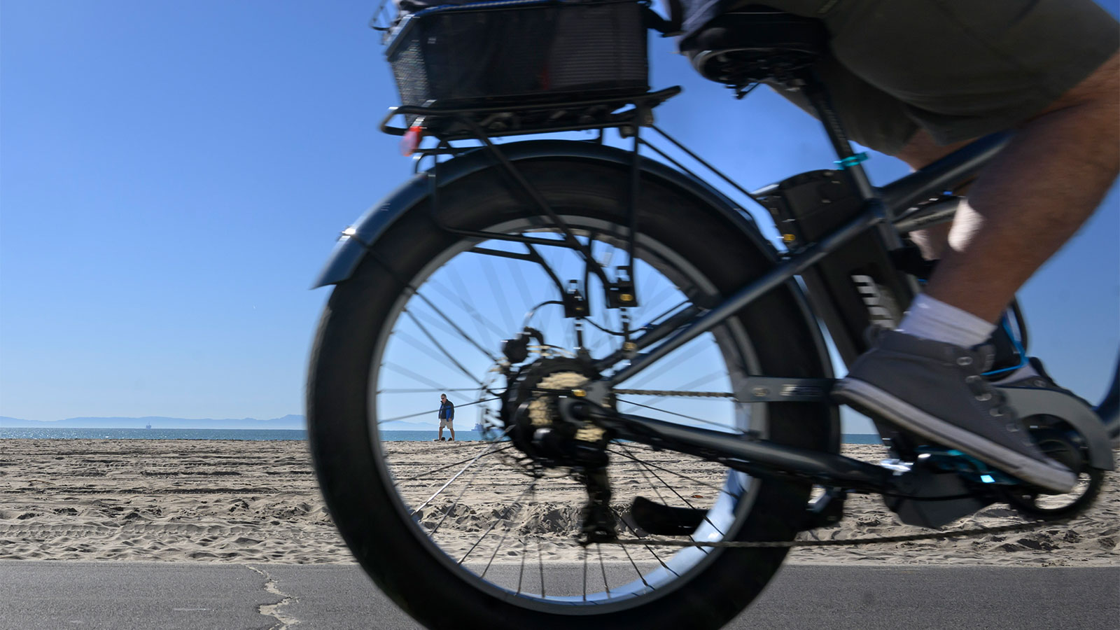 The rear tire of an e-bike is shown in front of a sandy horizon