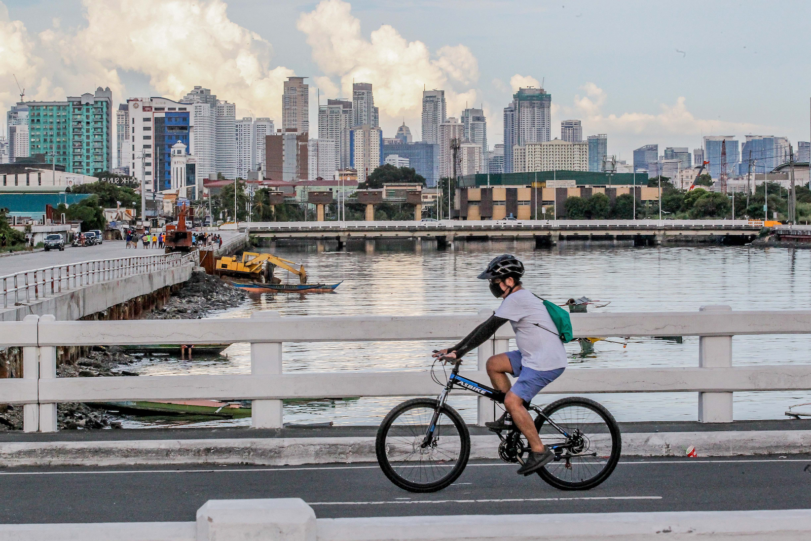 a person in a COVID mask rides a bike past a city near water