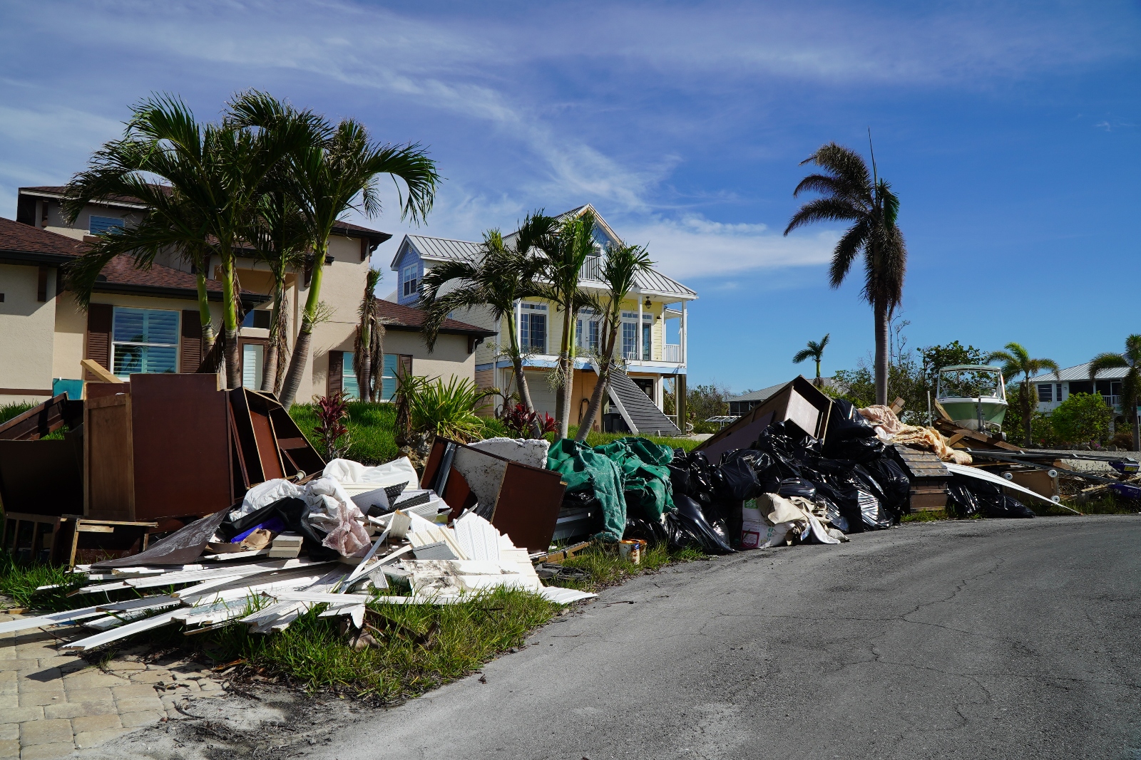 Piles of debris, including furniture, sit on the curb waiting to be picked up. A yellow building stands behind the debris – it was one of a few structures left standing in Fort Myers Beach after Hurricane Ian.