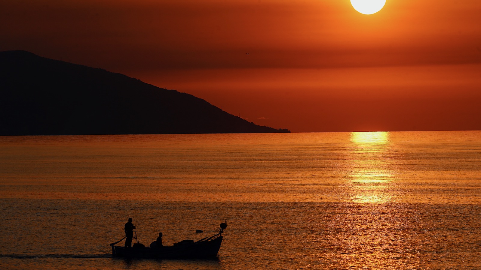 A small boat sails over the tranquil waters of the Black Sea at sunset.