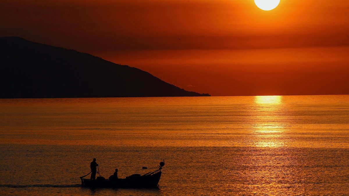 A small boat sails over the tranquil waters of the Black Sea at sunset.