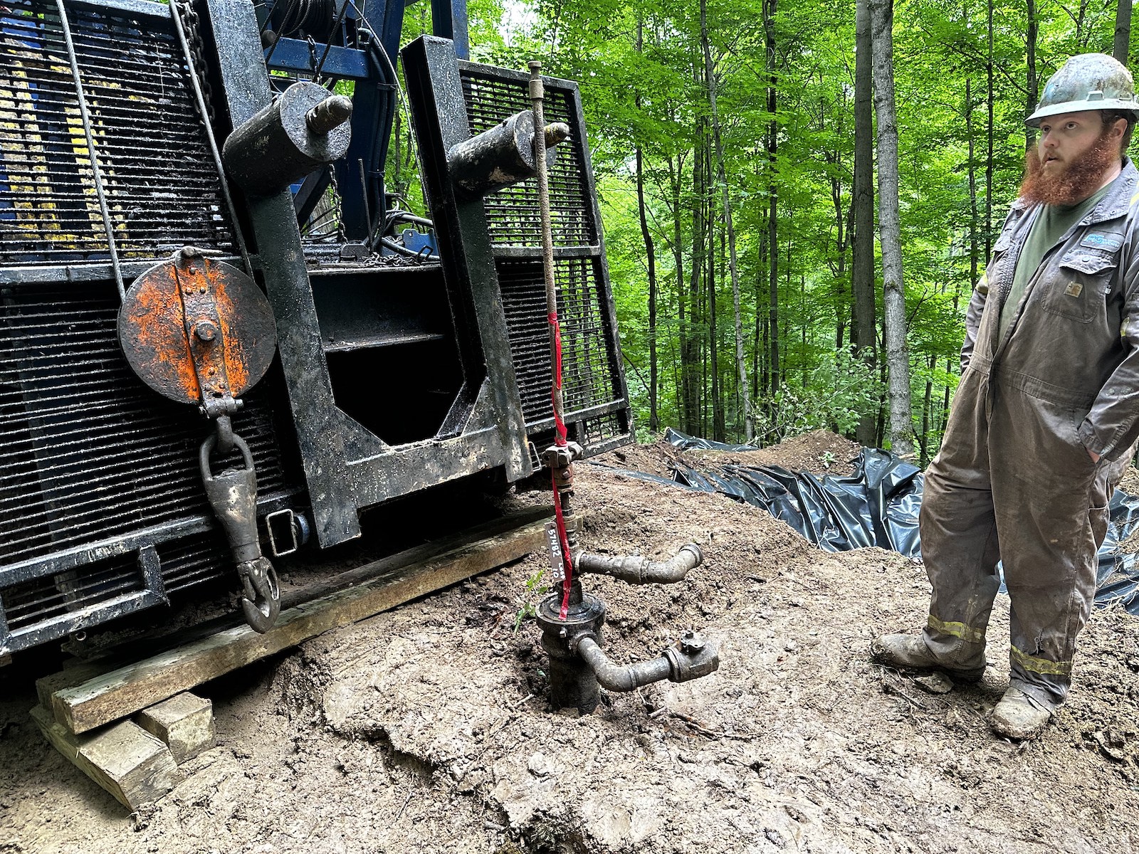 a man in a hardhat stands near well plugging equipment in a forest
