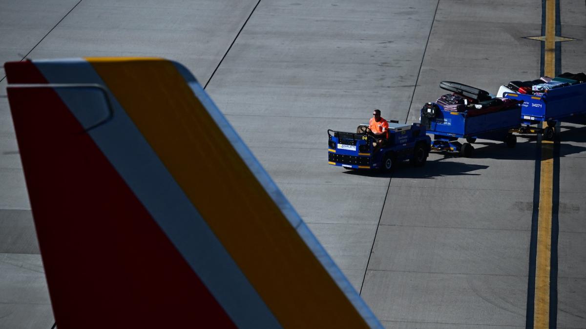A groundworker is seen driving a baggage cart heaped with luggage toward a jet parked on the tarmac at Phoenix Sky Harbor Airport.