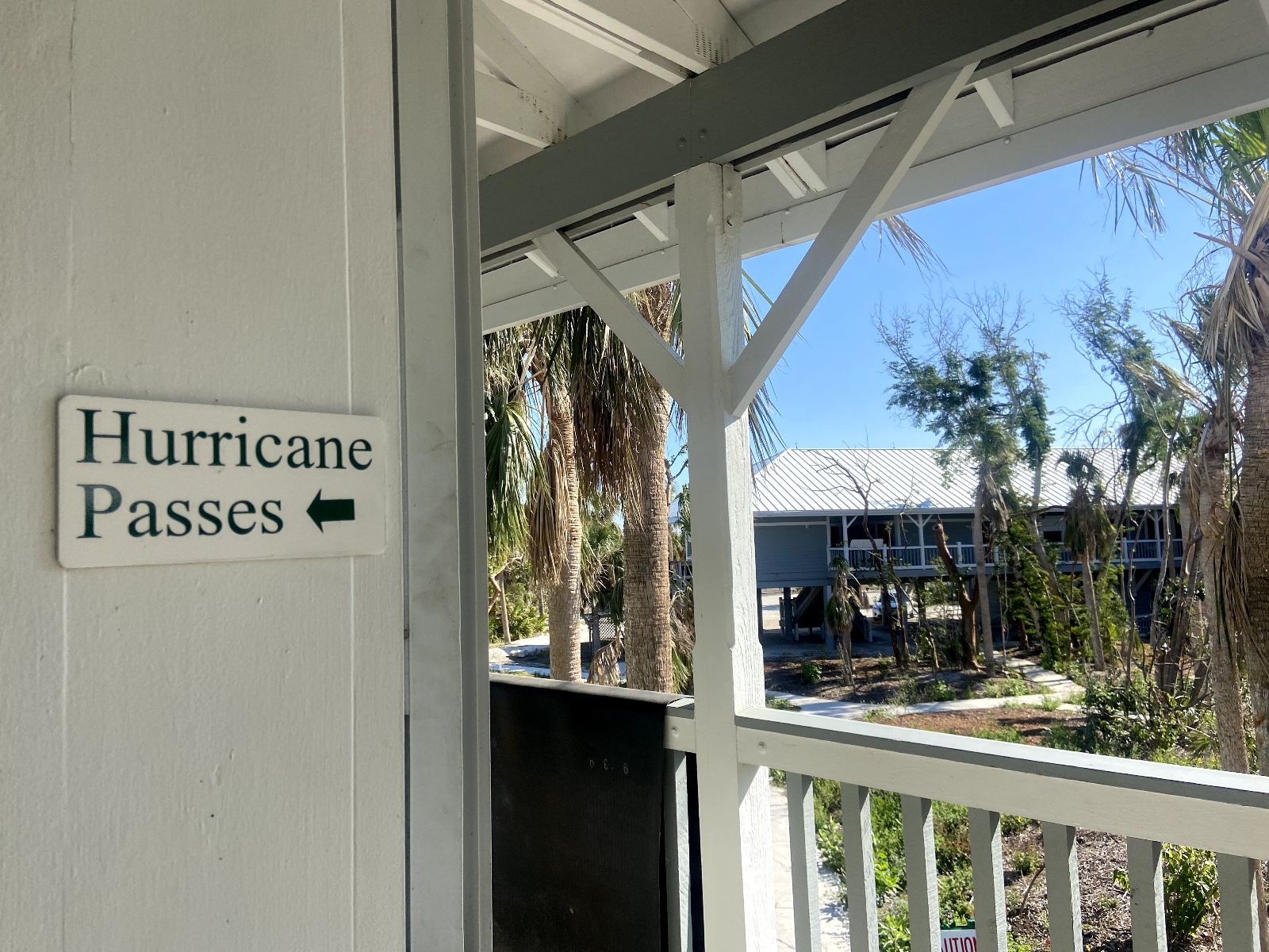 A white sign with black letters that reads “Hurricane Passes” hangs outside Sanibel City Hall. The damage from Hurricane Ian’s wind can be seen in the battered trees in the background. Sanibel officials limited access to the wealthy community by issuing hurricane passes to workers involved in the recovery effort.