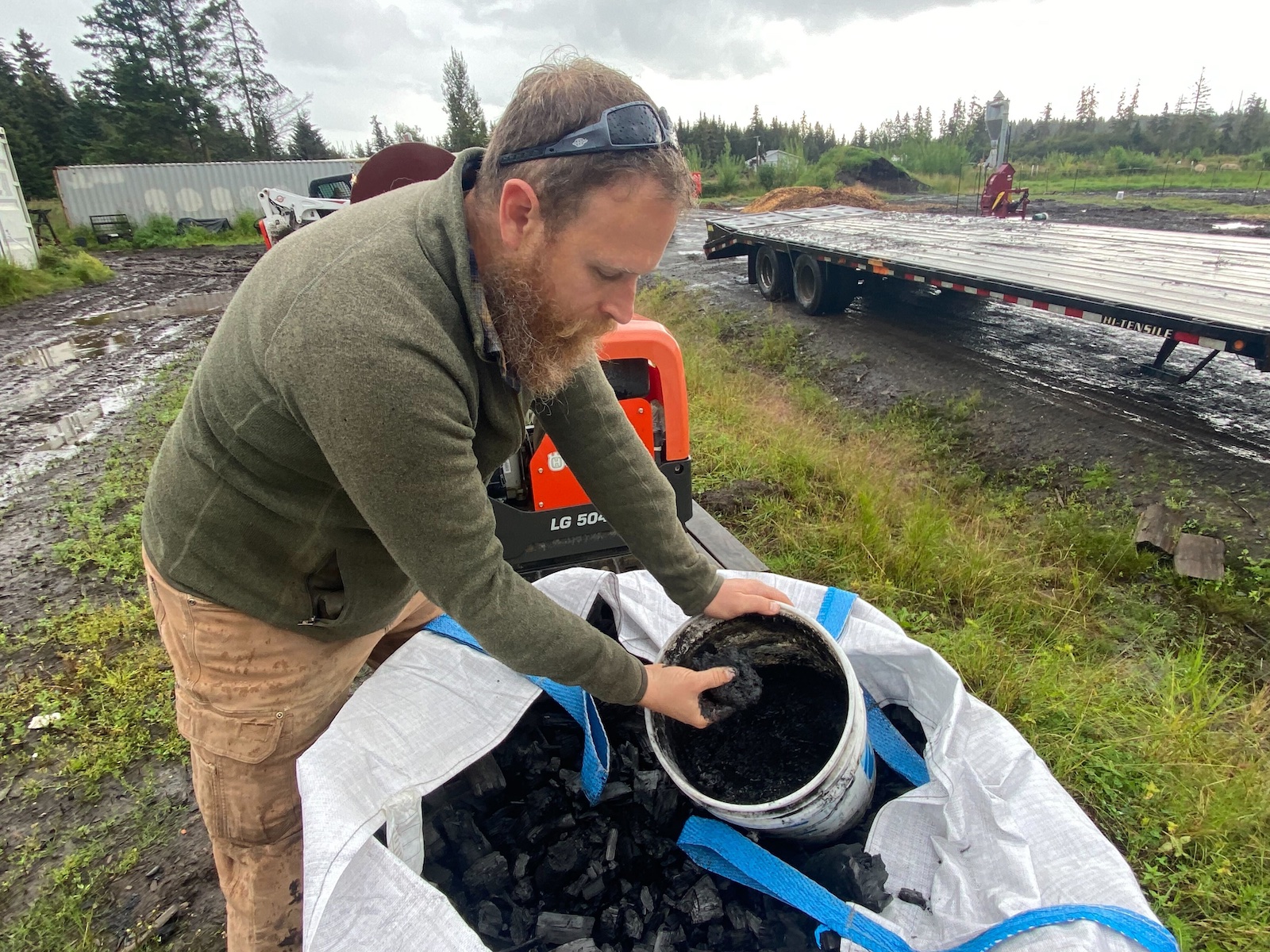 A farmer sticks his hand in a bucket of biochar at his farm in Alaska