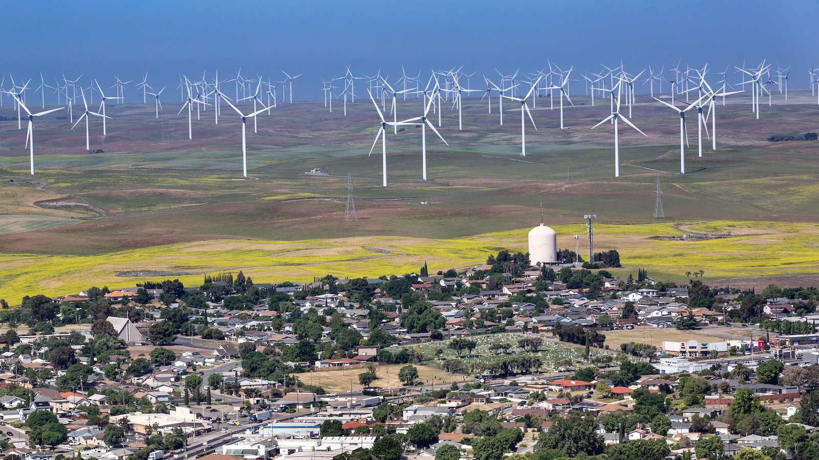 A vast field full of towering wind turbines is seen in the background with the small town of Rio Vista, California in the foreground.