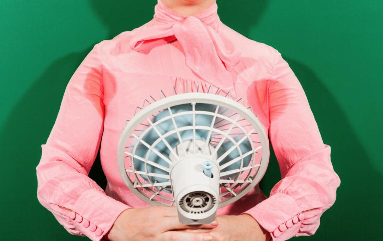 A 1950s-era woman pointing an electric fan on her sweating armpits