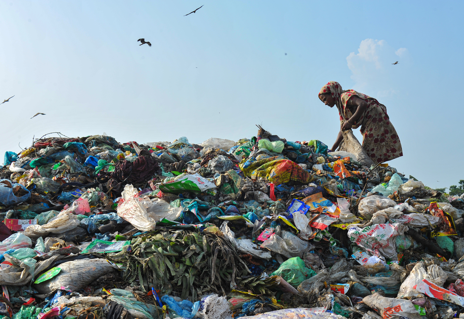 A woman picks up trash while standing atop a garbage heap