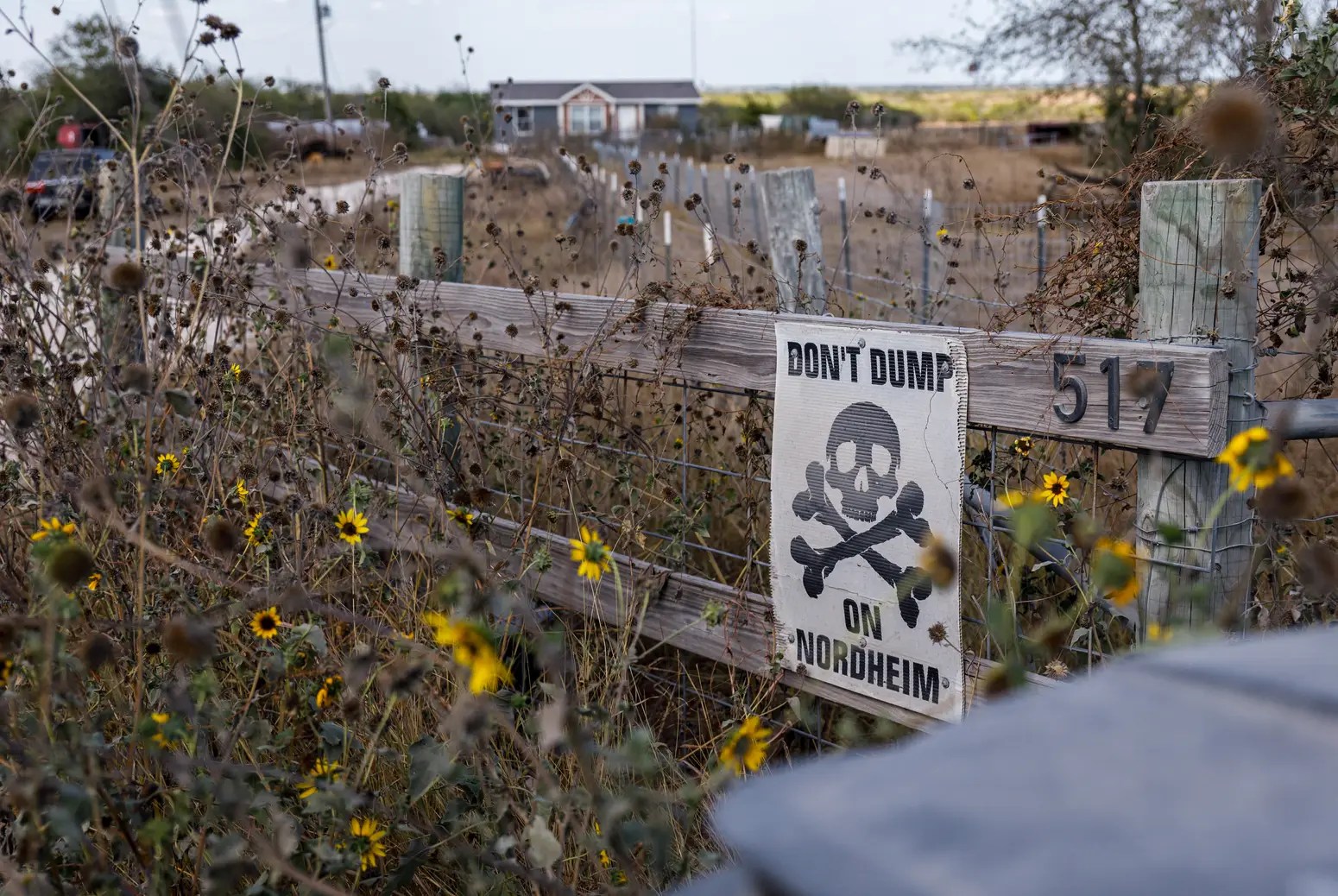 A wooden fence with yellow flowers poking out stands next to a sign that says "Don't dump on Nordheim."