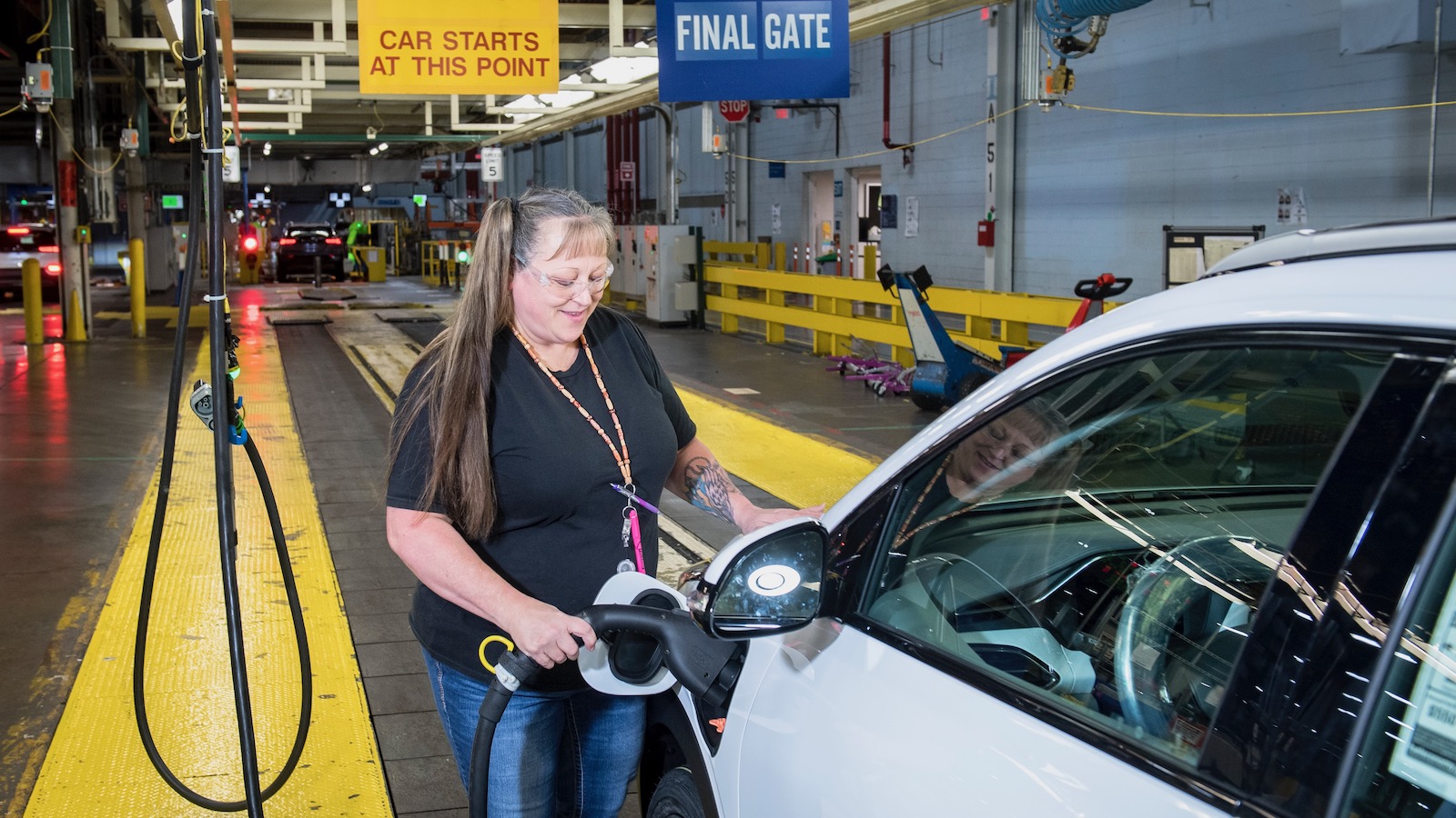 A factory worker on a General Motors assembly line plugs a charging cord into a Chevrolet Bolt electric vehicle.
