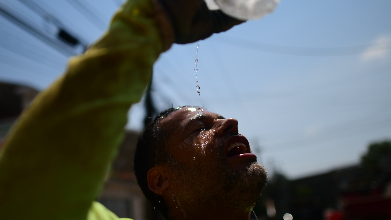 A man pours water on his face in the hot sun