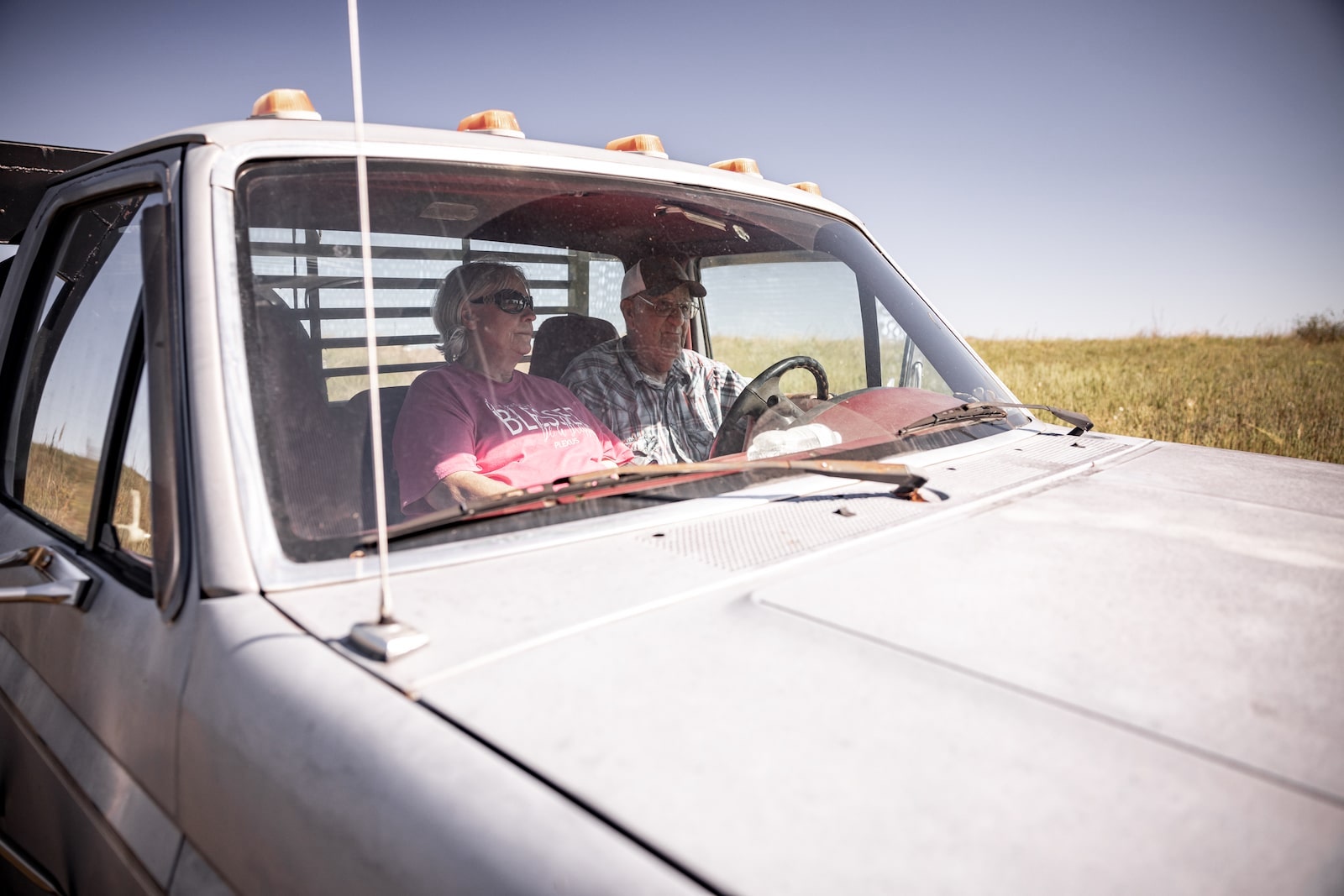 a man and a woman in their late 60s/early 70s drive a truck with a golden field in the background