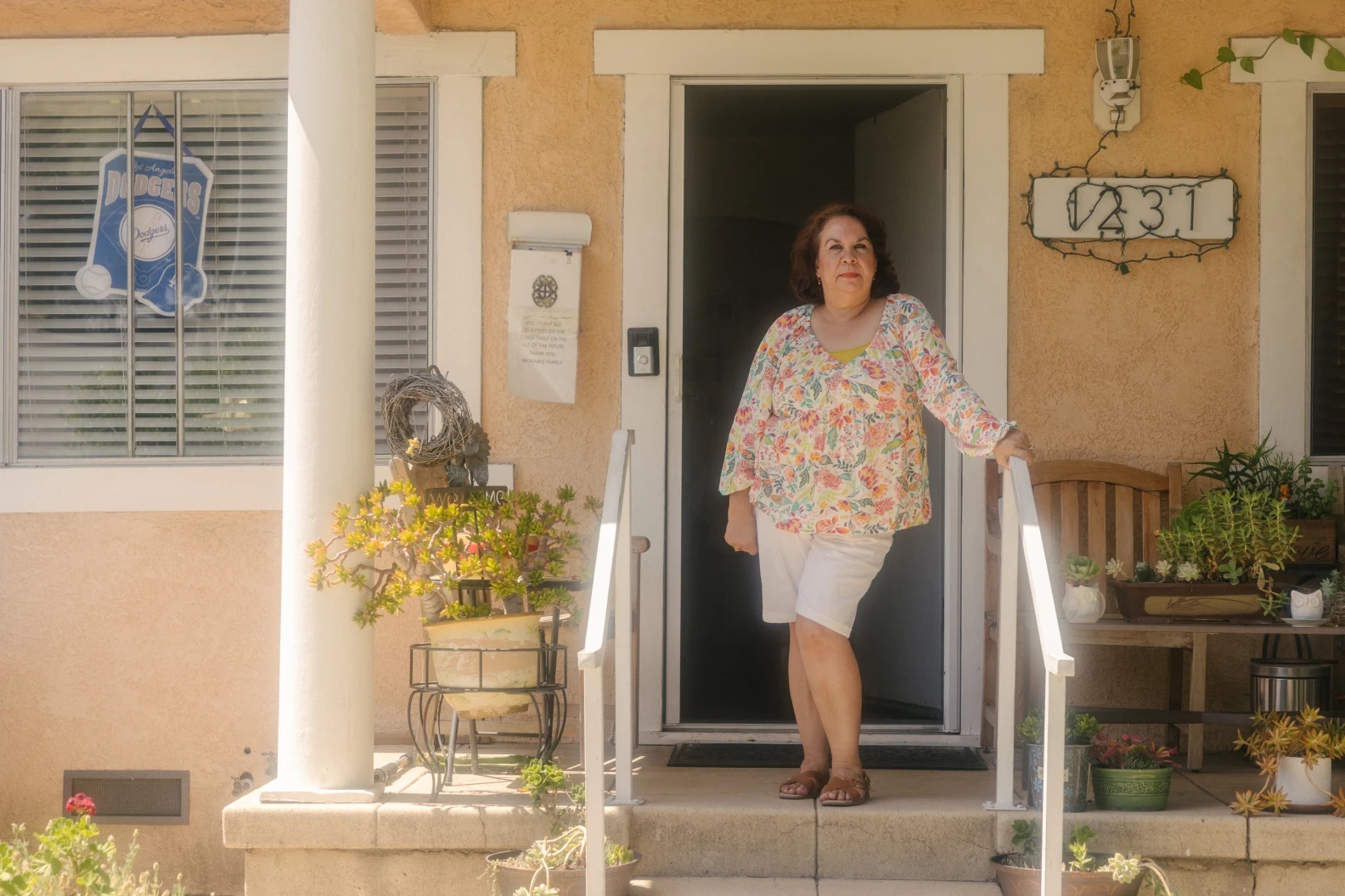 A woman in a flowery long-sleeved shirt stands in front of a home.