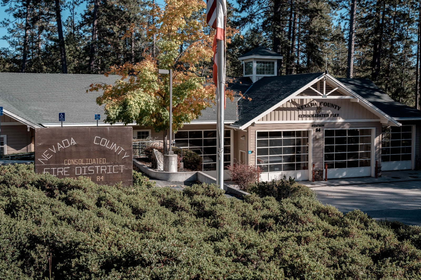 A building next to a tree and shrubs with a sign that says Nevada County Fire District.