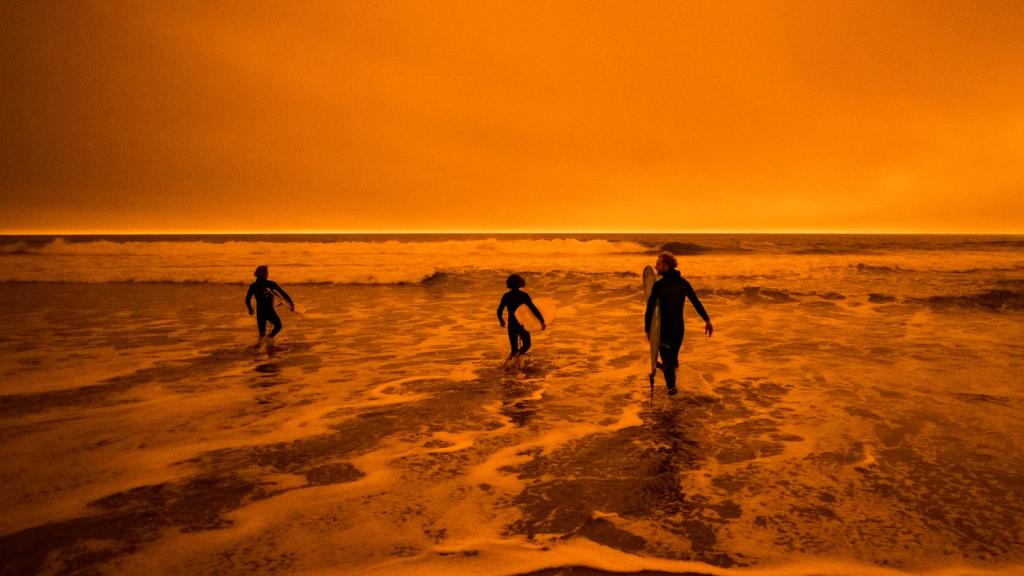 Children play in the ocean under an orange sky.