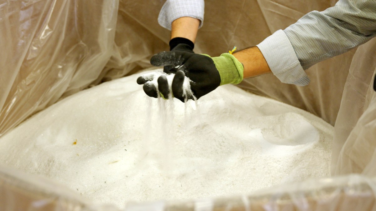 two gloved hands holding glass particles ground down to sand.