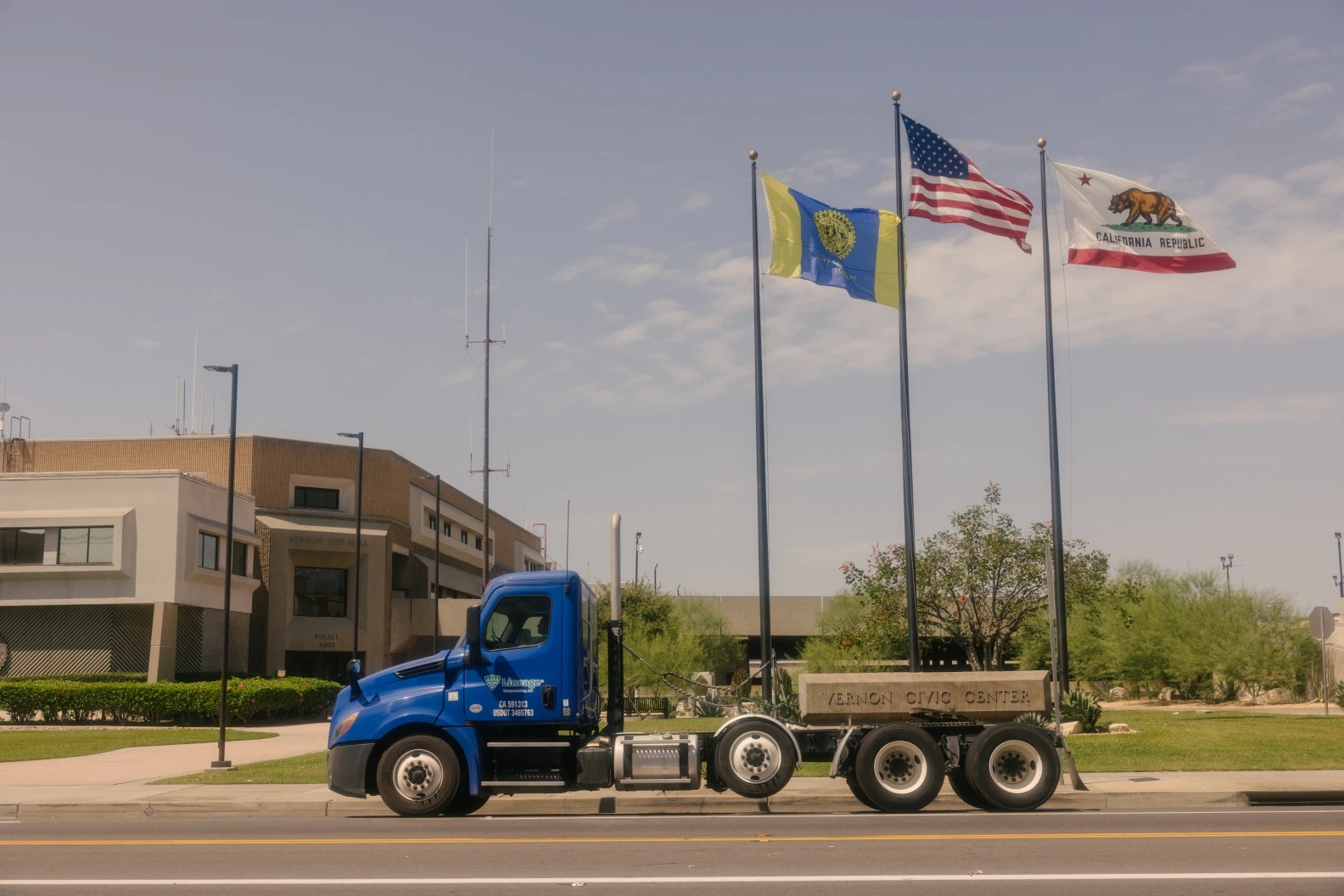 A blue truck passes by three flags.