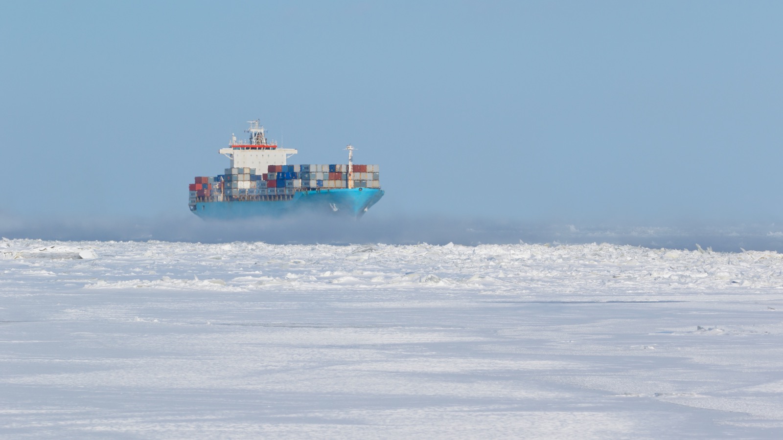 A cargo ship loaded with shipping containers traverses and ice passage.