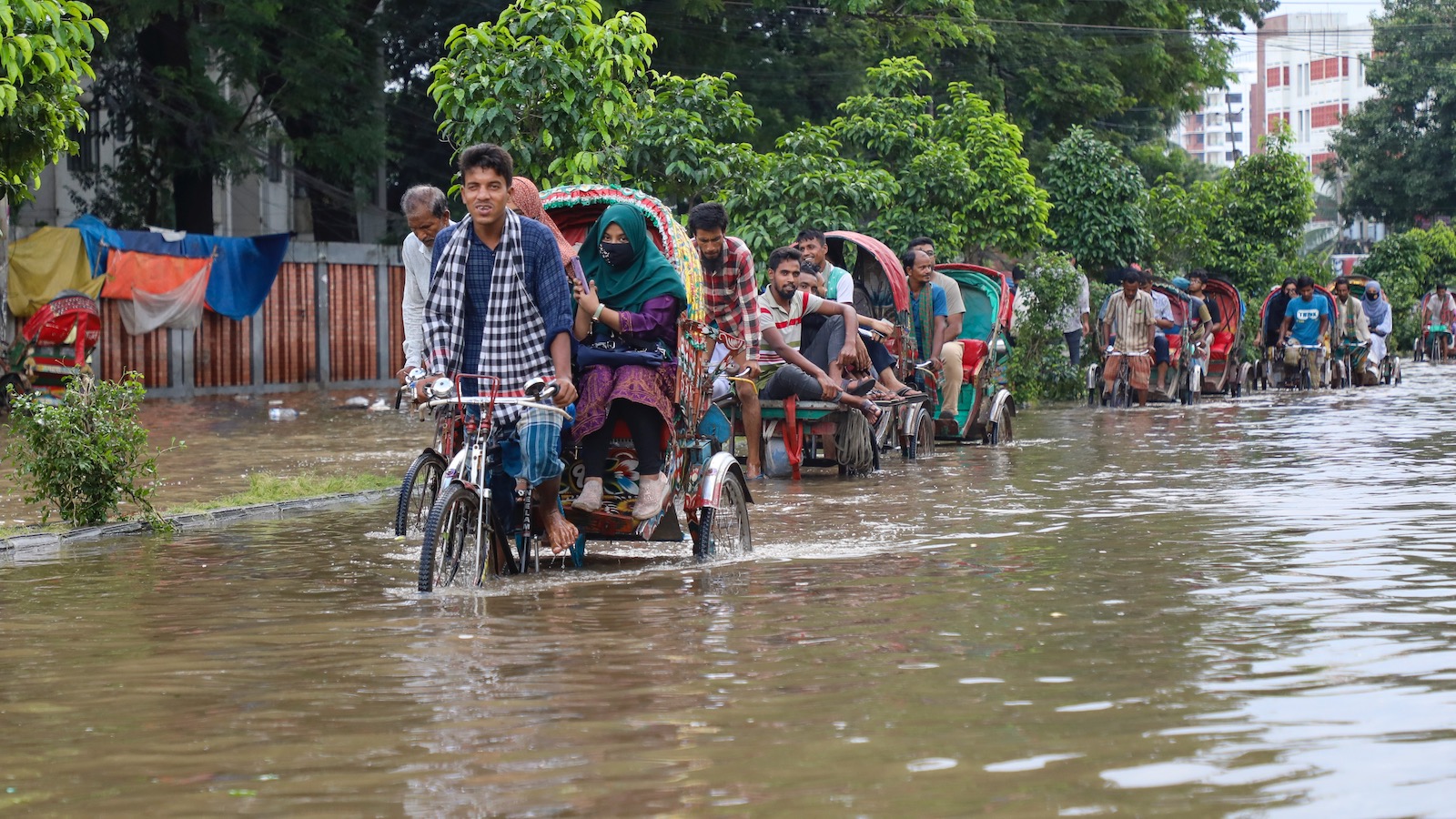 A long line of rickshaws pedals through the knee-deep waters of a flooded road in Bangladesh in September, 2023.