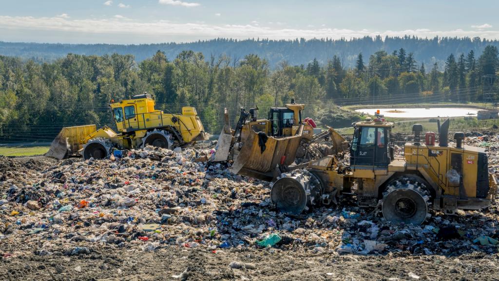 Tractors sit on top of a landfill, with forest in background