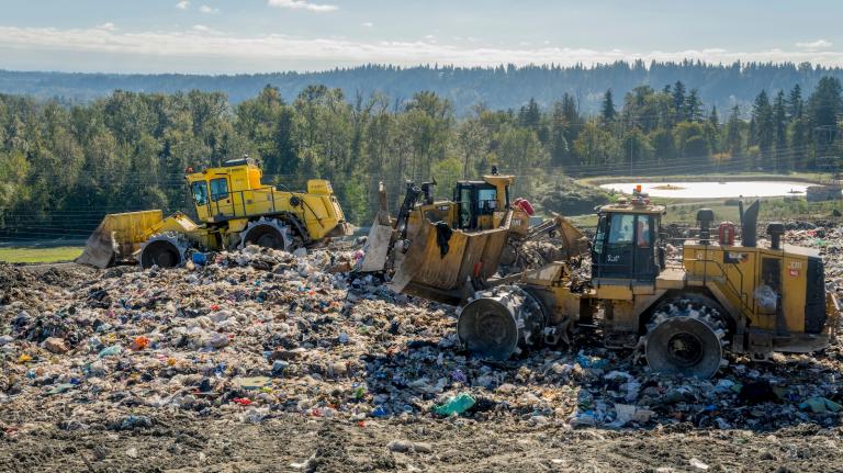 Tractors sit on top of a landfill, with forest in background