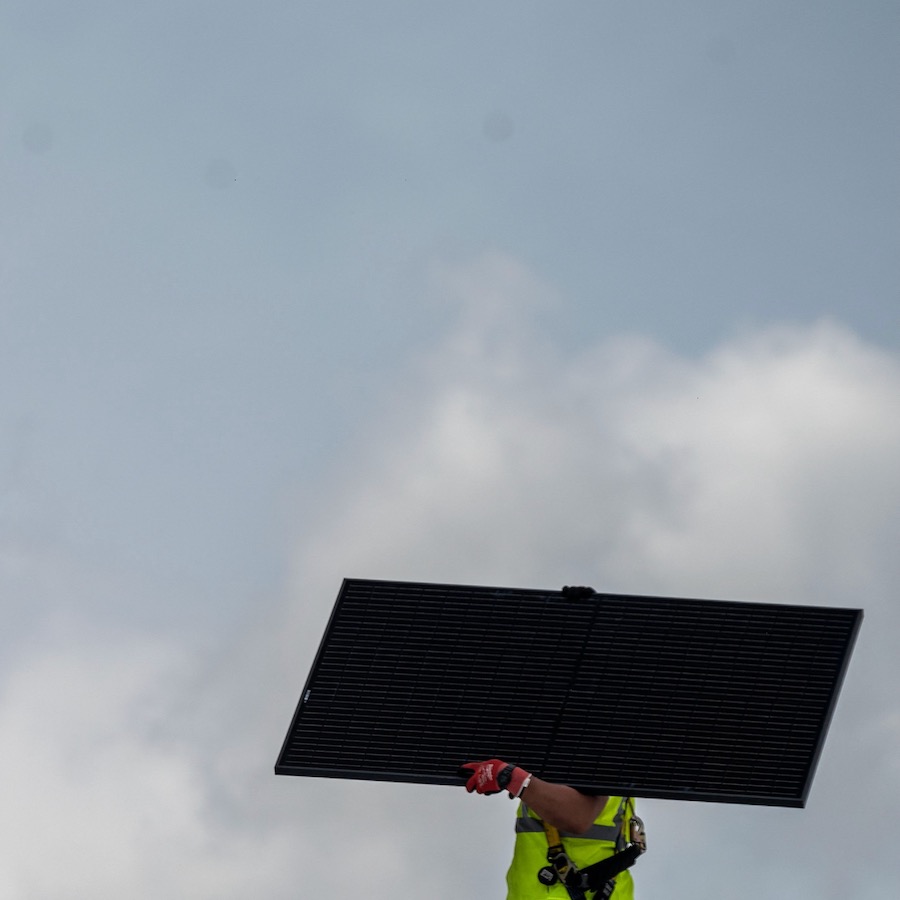 A man carrying a solar panel works on the roof of a church in Alexandria, Virginia.